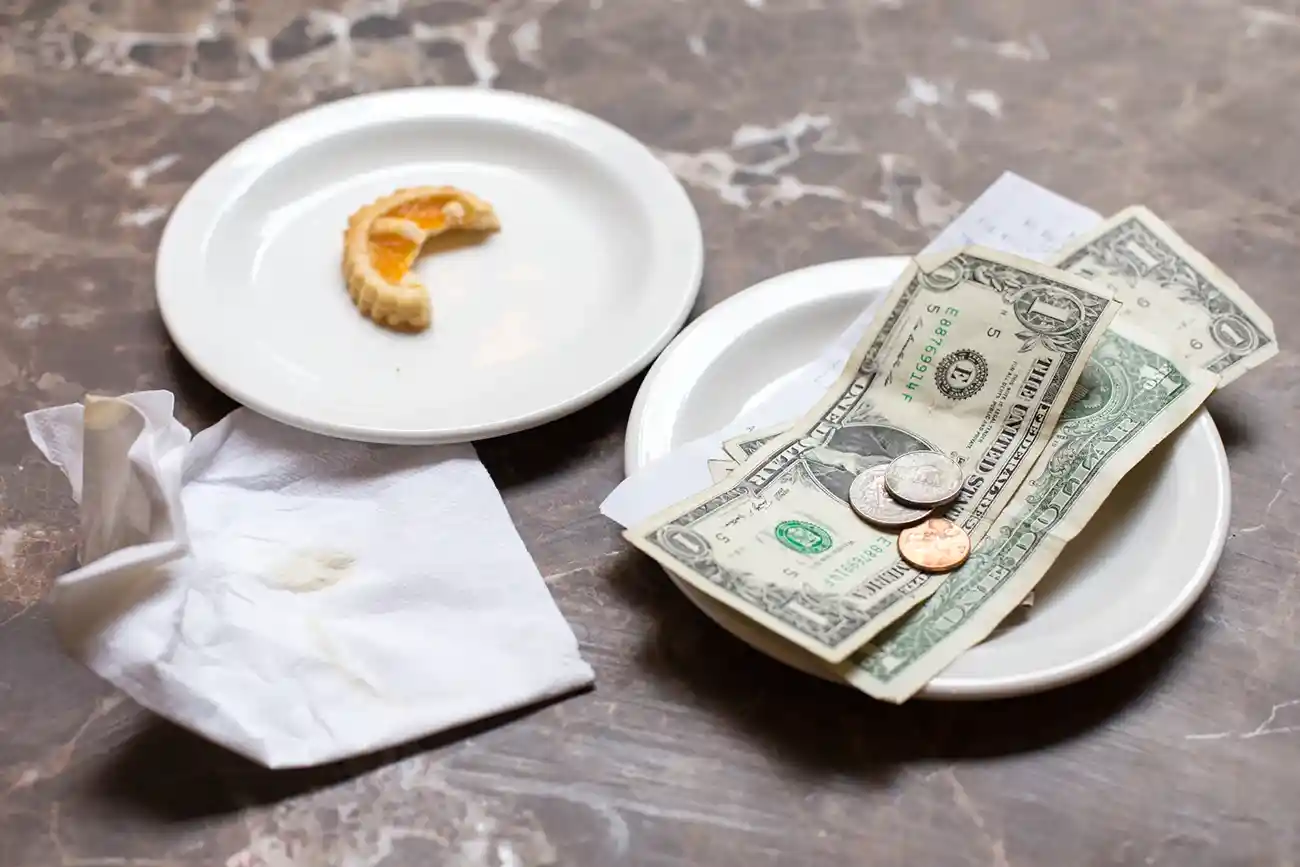 A hand placing dollar bills on a restaurant table, symbolizing the cultural and economic practice of tipping in the United States.