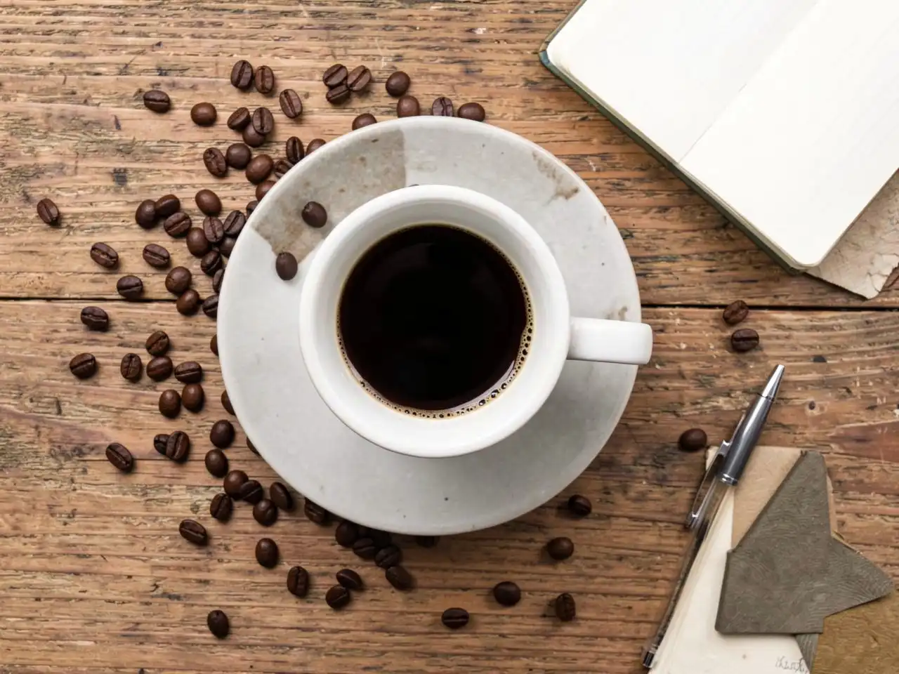 Top-down view of a coffee cup with steam, surrounded by scattered coffee beans on a wooden table