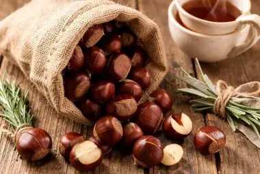 A rustic scene of fresh chestnuts in their shells spilling from a sack, with one cut open to reveal the creamy interior, symbolizing their natural, nourishing qualities.