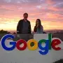 man and woman standing behind google logo with sunset background